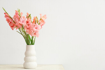 Vase with bouquet of beautiful gladiolus flowers on table against white background