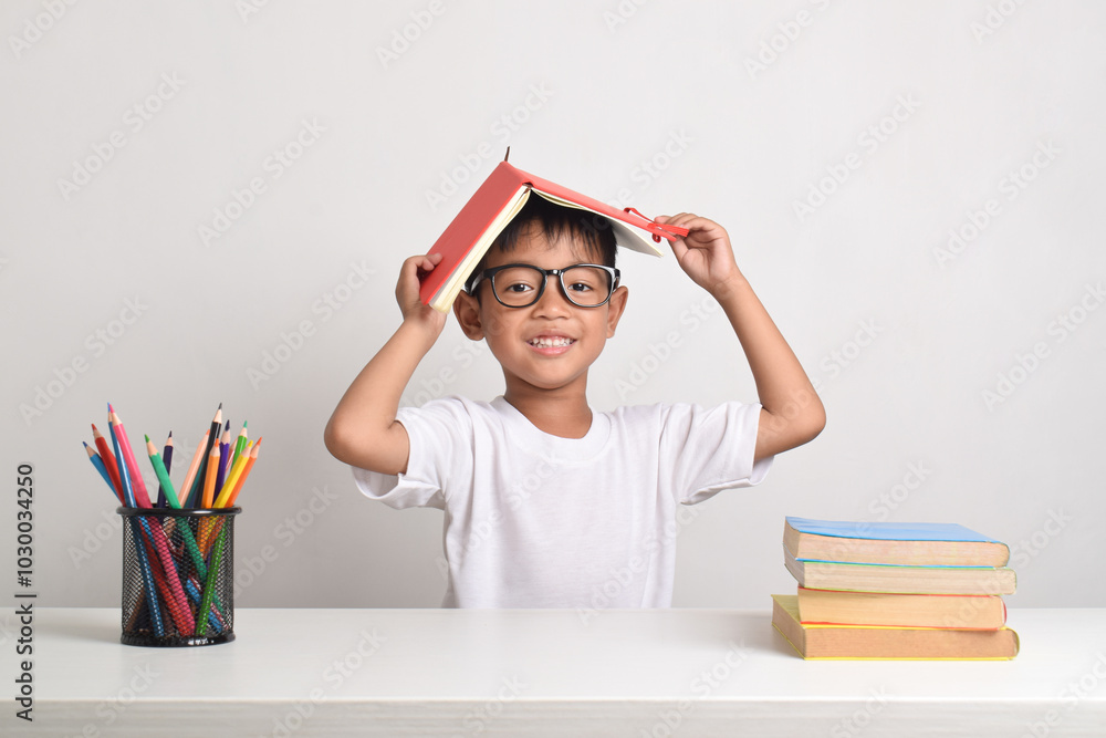 Portrait of an Asian boy studying with a book on his head isolated on a ...