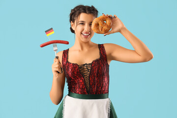 Wall Mural - Young Octoberfest waitress with pretzel and sausage on blue background