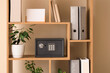 © Pixel-Shot - Modern safe, office folders and houseplants on shelving unit near beige wall