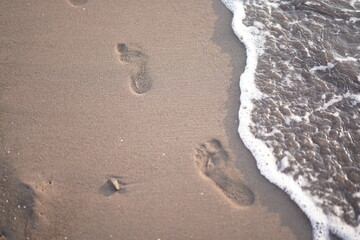 Footprints in the sand on the beach with sea wave background.