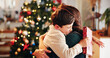 © Flashizzle/peopleimages.com - Christmas, gift and hug with mother, son and bonding together with decoration, house and festive in lounge. Xmas tree, family and parent with boy, embrace and present with happiness, holiday and love