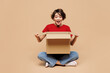 © ViDi Studio - Full body young surprised shocked happy woman she wear red t-shirt casual clothes sits unpacking hold cardboard box isolated on plain pastel light beige background studio portrait. Lifestyle concept.