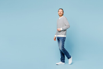 Wall Mural - Full body side profile view young happy man he wear striped sweatshirt casual clothes walk go look camera isolated on plain pastel light blue cyan wall background studio portrait. Lifestyle concept.