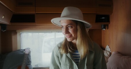 A young woman in a hat smiles looking at the camera while sitting on a bed in a van