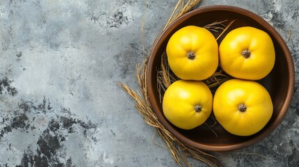 Wall Mural - Four bright yellow apples in a brown bowl with straw, on a gray background.