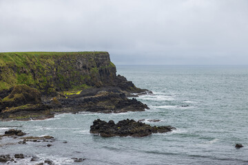 the rugged basalt cliffs of bay of the cow meet the atlantic ocean, with overcast skies near giant's
