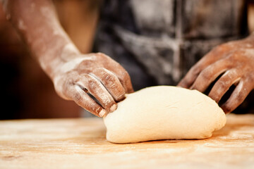 Person, hands and baker kneading with dough for bread, rolls or pastry production on wooden table. Closeup, chef or bakery with flour, ingredients or wheat for handmade food or heast at factory