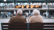 © forenna - Elderly couple sitting together on a bench in a train station waiting area, sipping coffee while reading the departure board photo