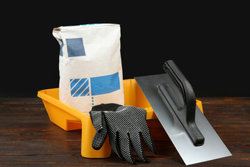 Sticker - Bag of cement powder, tray, putty knife and rubber glove on wooden table. Building material and construction tools