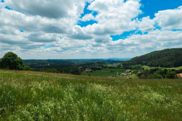 Beautiful landscape with rolling green hills, clear blue sky with fluffy clouds, and distant mountain of Schoeckl seen from Mariatrost, Graz, Styria, Austria, Europe. Field of tall grass in foreground