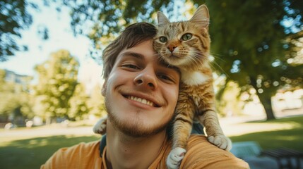 A young man beams with joy as he poses outdoors, his cat playfully resting on his shoulder under the sun