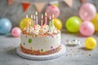 © MohdAdzmer - A festive birthday cake with colorful candles and sprinkles with balloons at the back