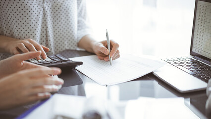 Woman accountant using a calculator and laptop computer while counting and discussing taxes with a client. Business audit concepts