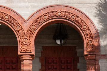 Two large red clay decorative exterior archways on a grey brick building. The vintage Spanish style architecture has decorative columns, trim and details in the arches.The opening leads to a courtyard