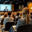 © Tadeusz - Focused woman attending a conference seminar with a large audience in the background.