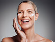 © KayExam/peopleimages.com - Laugh, mature woman and skincare cream for hydration, moisturizer and beauty cosmetics. Lotion, happy model and hand for facial dermatology, collagen or glow for anti aging on gray studio background