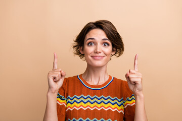 Wall Mural - Photo portrait of pretty young girl pointing up empty space wear trendy orange print outfit isolated on beige color background