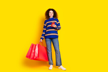 Wall Mural - Full size photo of lovely girl dressed sweater holding shopping bags smartphone read notification isolated on yellow color background