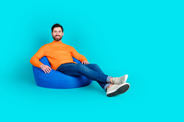 Photo of cheerful positive nice man wear trendy clothes sit pouf empty space isolated on cyan color background