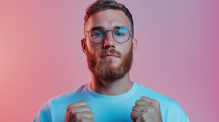 A confident young man with a beard and glasses strikes a serious pose. The casual attire and vibrant background create a modern and stylish look, showcasing determination and personality.