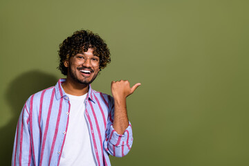 Wall Mural - Photo of handsome arabian recruiter in striped casual shirt and eyeglass pointing finger vacancy salary isolated on khaki color background