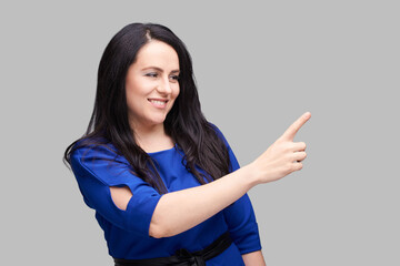 Confident woman pointing in blue dress on gray background for business concept.