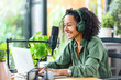 © ximich_natali - Smiling woman in green shirt with voluminous hair, podcasting at home with laptop and microphone. Modern online communication, blogging