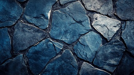 Textured blue stone wall with irregular shapes and cracks, creating a mosaic-like pattern. Natural rock surface with deep shadows enhances depth and dimension.