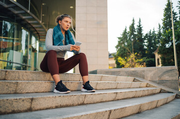 Wall Mural - Young sporty woman using smartphone after training outdoors