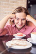 © elenavolf - Cheerful woman enjoying coffee and desserts in cafe setting with macarons and cake.