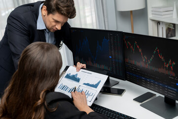 Two business traders discussing value business statistic graph company on paper report analyzing with dynamic stock exchange market currency real time website surround pc screens at office. Postulate.