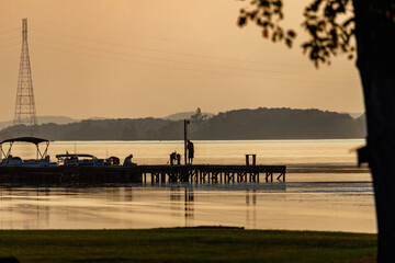 a pier with people fishing is silhouetted against a lake at dusk