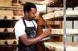 © HockleyM4/peopleimages.com - Black man, tablet and baker check stock, inventory or bread proofing basket on shelf. Technology, bakery and chef in factory for manufacturing, food production or quality inspection in small business