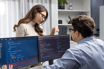 Wall Mural - woman colleague standing opposite to man programmer working on desk to discuss coding website softwa