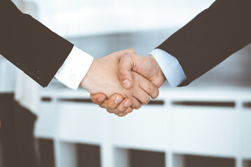 Businessman and woman shaking hands with colleagues at the background. Handshake at meeting in office. Concept of success in business