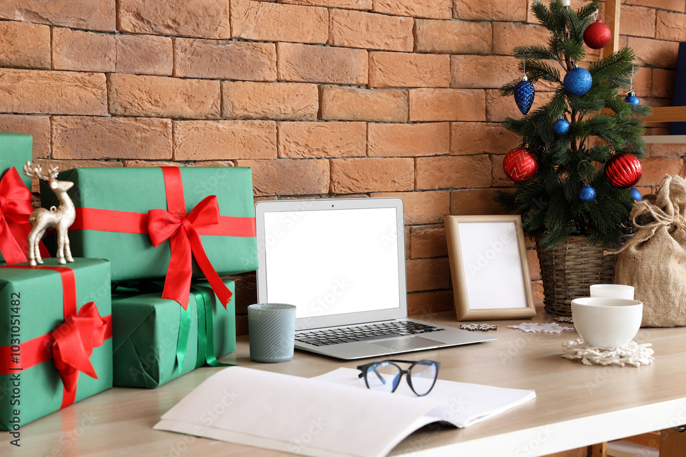 Modern workplace with blank laptop, presents and Christmas tree in office