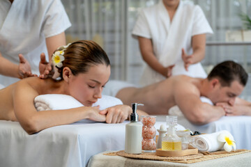 Caucasian couple customer enjoying relaxing anti-stress spa massage and pampering with beauty skin recreation leisure in day light ambient salon spa at luxury resort or hotel. Quiescent