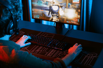 Host channel of young gaming streamer, team gamer playing battle game with multiplayer at warship on pc screen with cropped back side image, wearing headset with mic at digital neon room. Gusher.