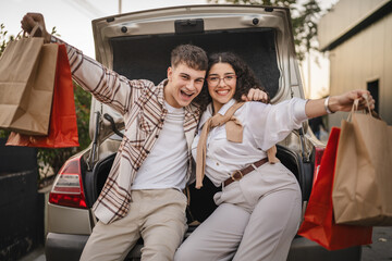 young adult costumer couple with shopping bags sit in car trunk