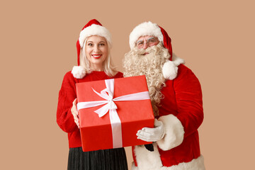 Sticker - Santa Claus and beautiful mature woman in Christmas hats with gift box on brown background