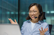© Liubomir - Asian businesswoman wearing headset engaged in online meeting. Smiling, gesturing while looking at laptop in professional office. Concept of virtual communication, technology, connection