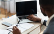© Prostock-studio - Unrecognizable black businessman working on laptop with blank screen on his workplace in modern office interior. Over shoulder shot, selective focus on device