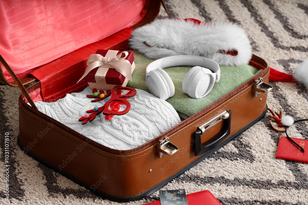 Suitcase with clothes, headphones, Christmas gift and decor on carpet
