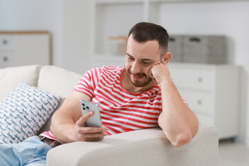 Poster - Handsome man using smartphone on sofa indoors