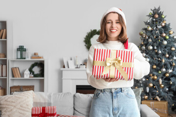 Wall Mural - Young woman in Santa hat with Christmas gift box at home