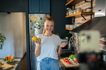 Smiling young woman cooking and filming with smartphone in modern kitchen