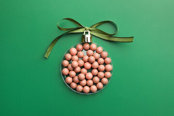 Wall Mural - Christmas ball made of cosmetic product and bow on green background, top view