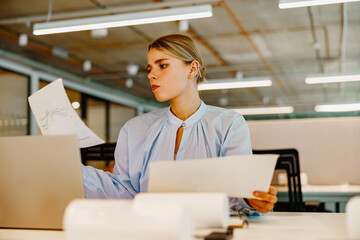 Wall Mural - A young professional diligently assessing various documents with focused attention in a stylish contemporary workspace