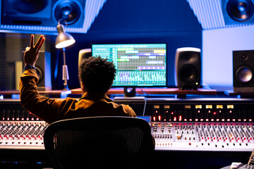 Fototapete - Sound designer counting down for artist to sing in sound booth, showing a sign to let the singer know when to start the performance. Music producer operating control desk panel board.